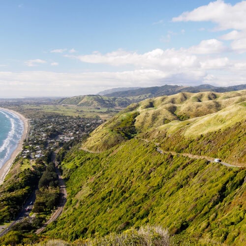 Vibrant coastal landscape of Paekākāriki, New Zealand, showcasing lush green hills, scenic winding road, and stunning ocean views, ideal for tourism and outdoor adventures.