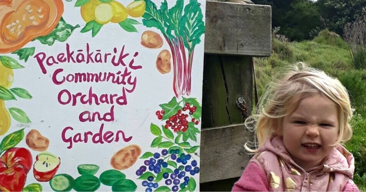 Paekakariki Community Orchard and Garden painted sign with a child sitting next to you