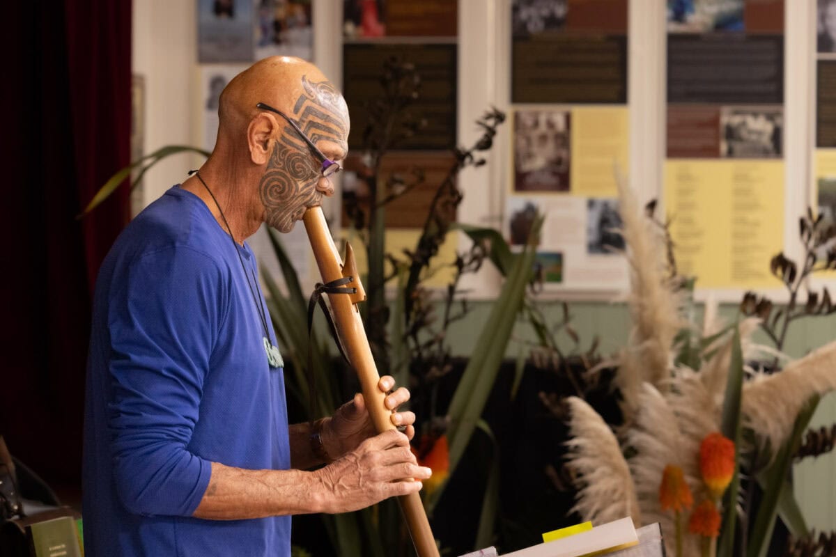 A man playing a traditional Māori taonga pūoro (wooden flute) at an indoor cultural event, showcasing Māori music and heritage in Paekākāriki, New Zealand.