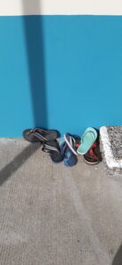 Flip-flops and sandals lined up against a bright turquoise wall in Paekākāriki, a coastal village in New Zealand. Perfect for beach days, showcasing relaxed seaside footwear and vibrant coastal colors.